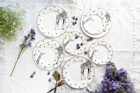 Top-down view of multiple white bone china dinner and quarter plates featuring black and white giraffe illustrations and star borders