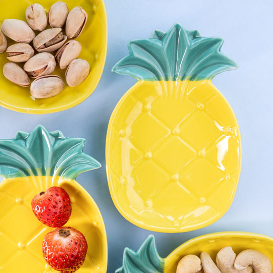 Close-up view of multiple yellow pineapple-shaped bone china snack plates with green crowns