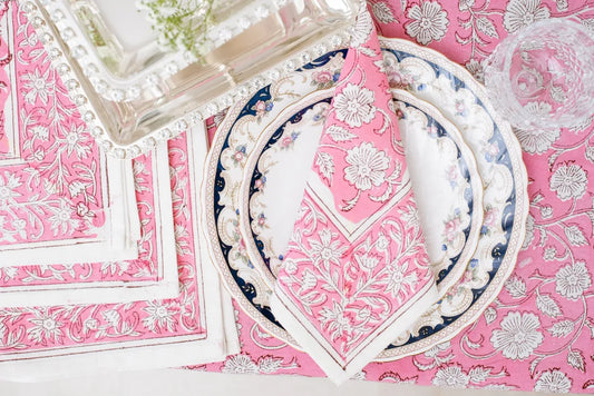 A square pink cotton napkin featuring a white Rajasthani floral block print pattern and a thin white border