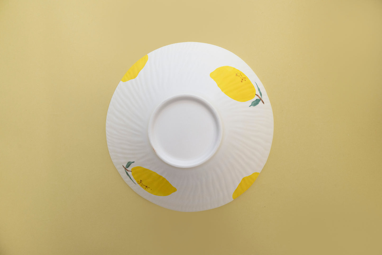 Bottom view of an upside-down white stoneware salad bowl featuring a yellow lemon pattern