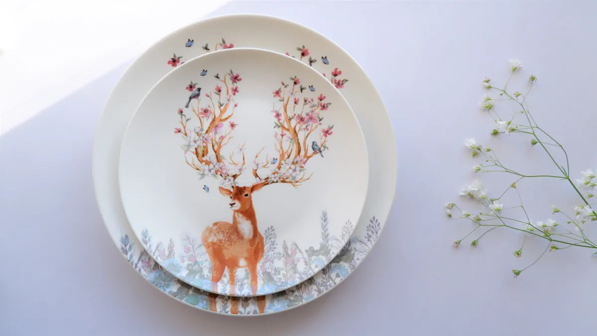 A top-down view of a small bone china quarter plate nested inside a larger matching dinner plate, both featuring a vintage deer and floral horn design
