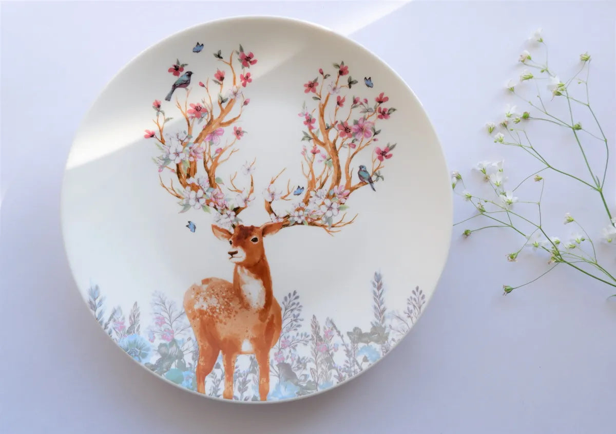 A top-down view of a white bone china dinner plate featuring a vintage deer illustration with vibrant pink and blue floral horns