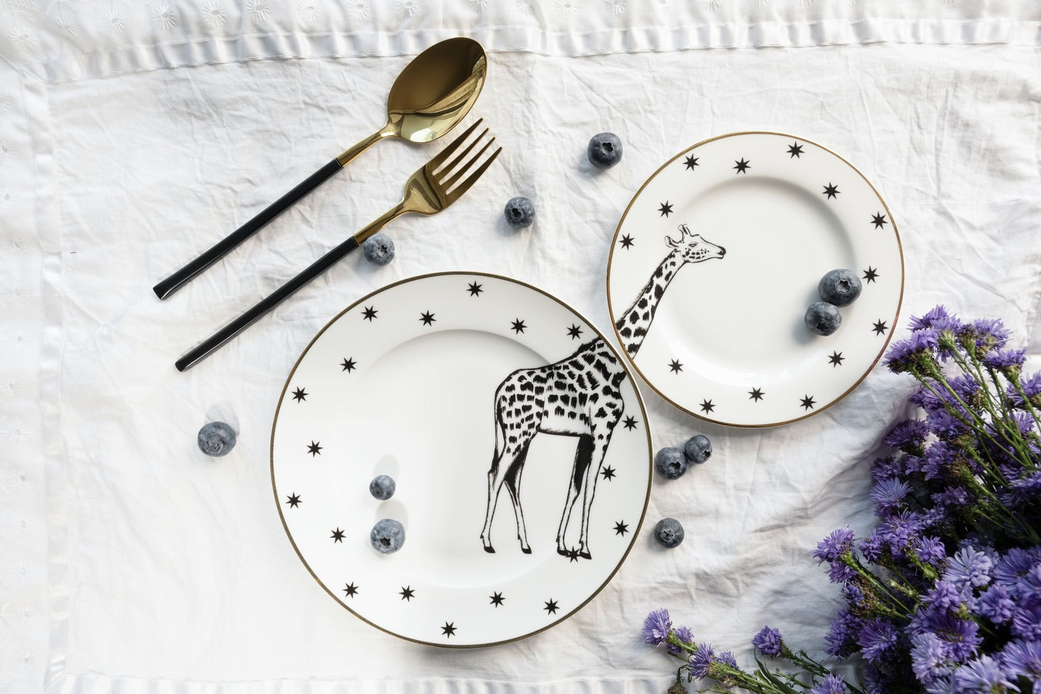 Top-down view of one white bone china dinner plate and one matching quarter plate, both featuring black and white giraffe illustrations and star borders