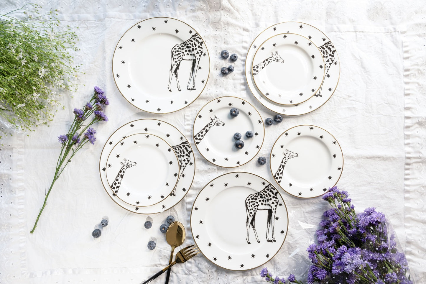 Top-down view of multiple white bone china dinner and quarter plates featuring black and white giraffe illustrations and star borders