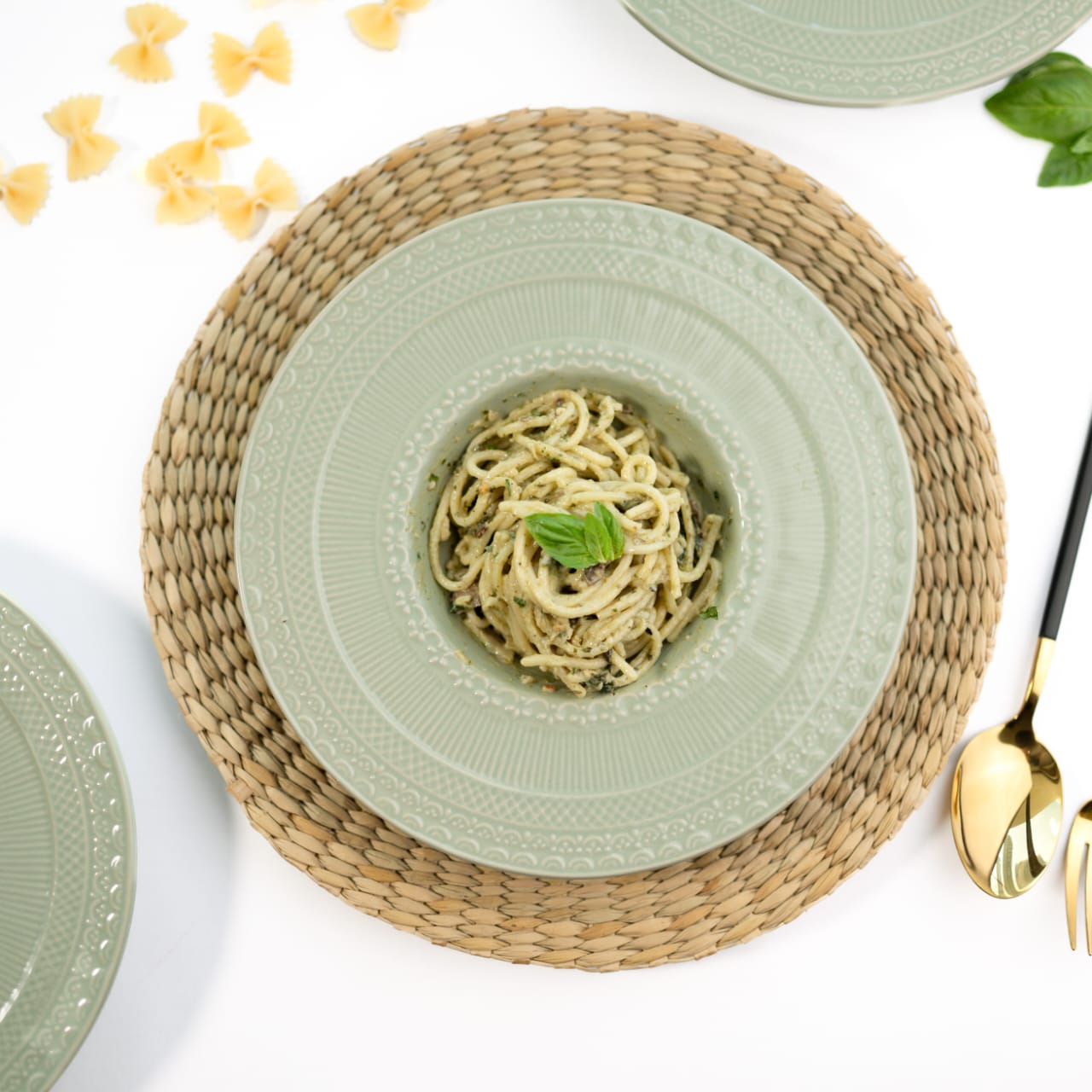 Angled top-down view of a jade green bone china pasta plate with ornate engraved rim patterns
