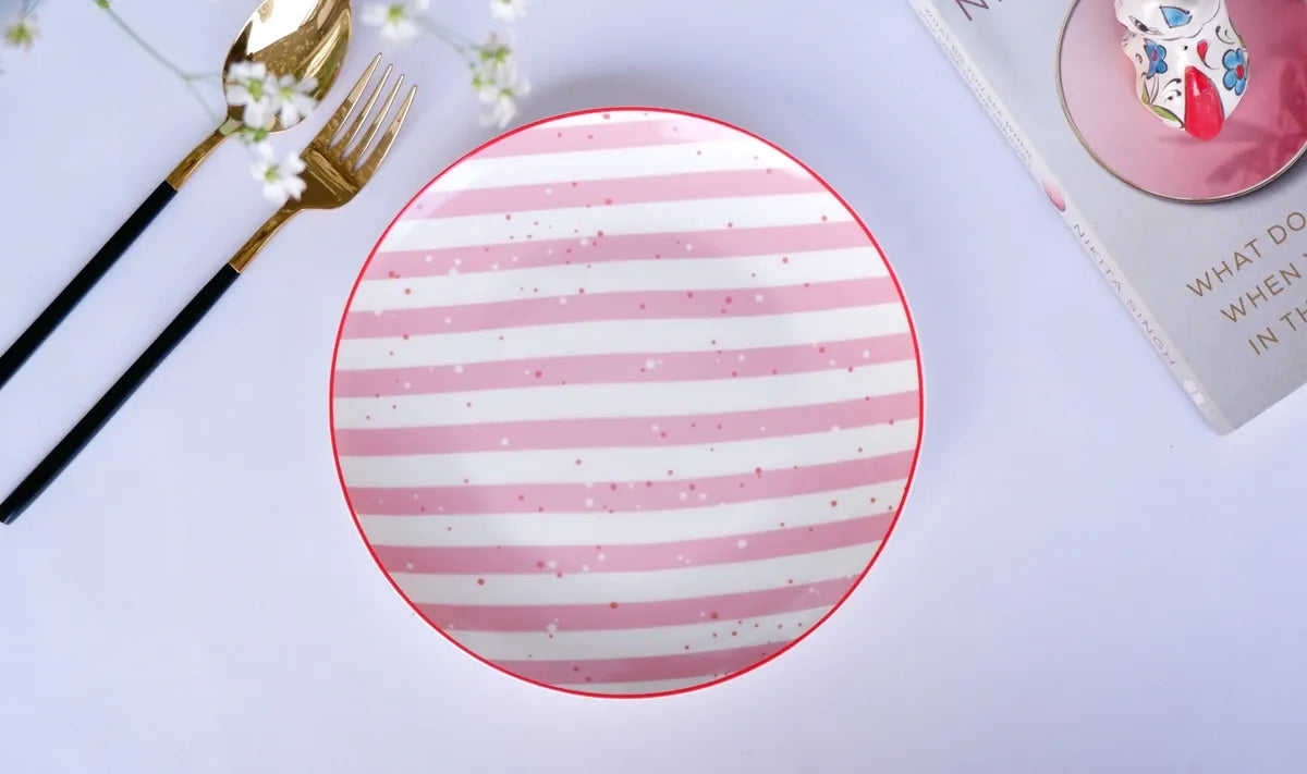 Top-down lifestyle view of a round white bone china quarter plate with pink and white horizontal stripes and a red rim