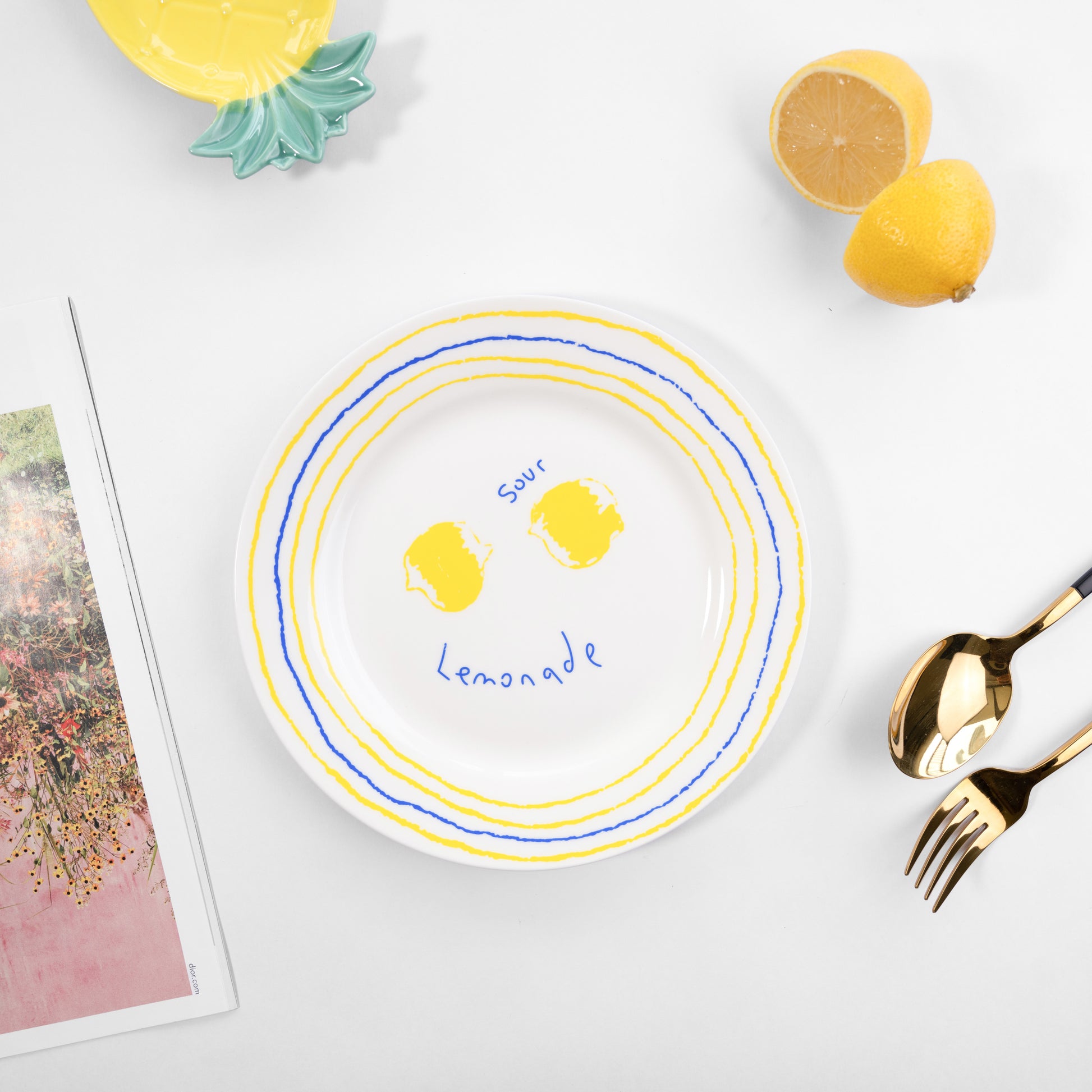 Top-down view of a white bone china quarter plate in the Lemonade style featuring two yellow lemons and blue and yellow circular borders