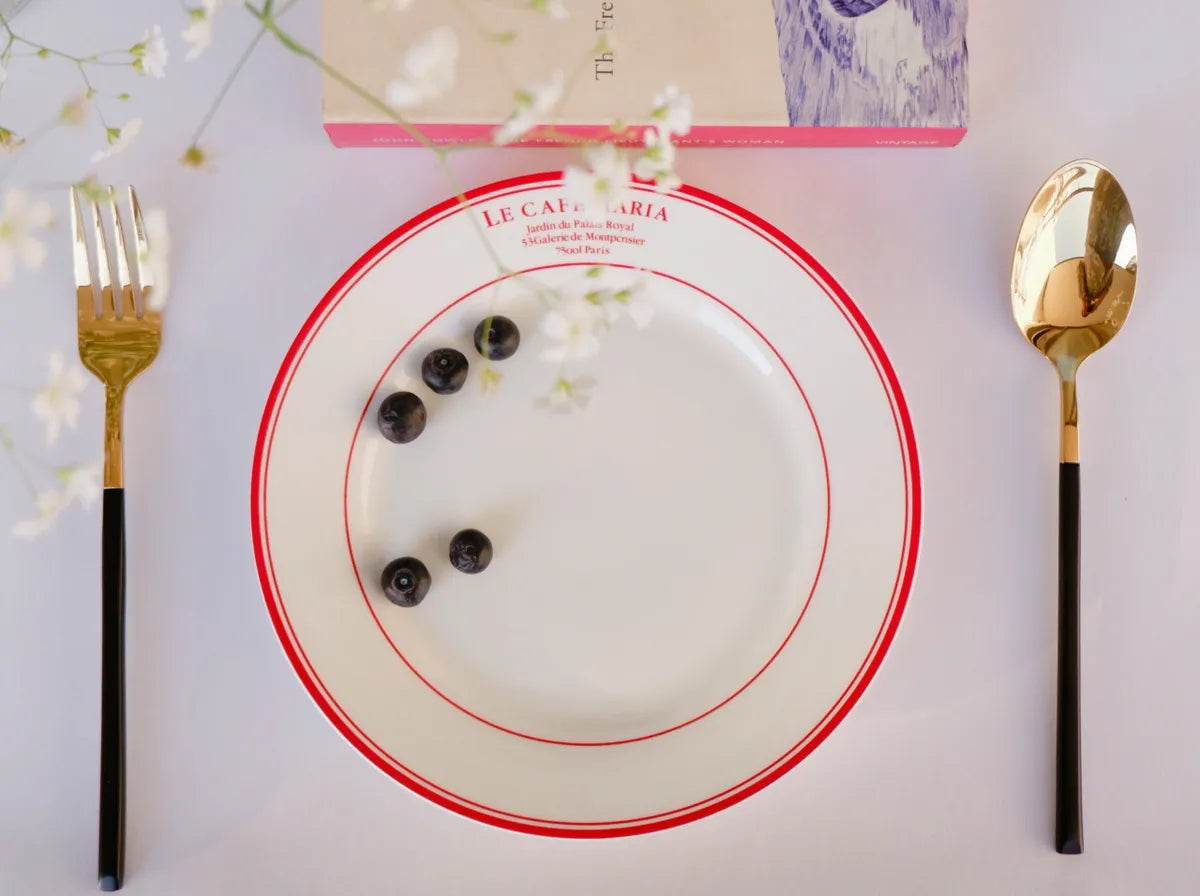 Top-down view of a white bone china quarter plate featuring red double circular borders and red "Le Cafe Maria" branding