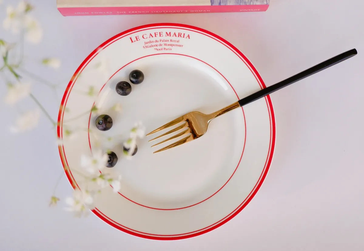 Top-down view of a white bone china quarter plate with double red circular borders and red "Le Cafe Maria" branding