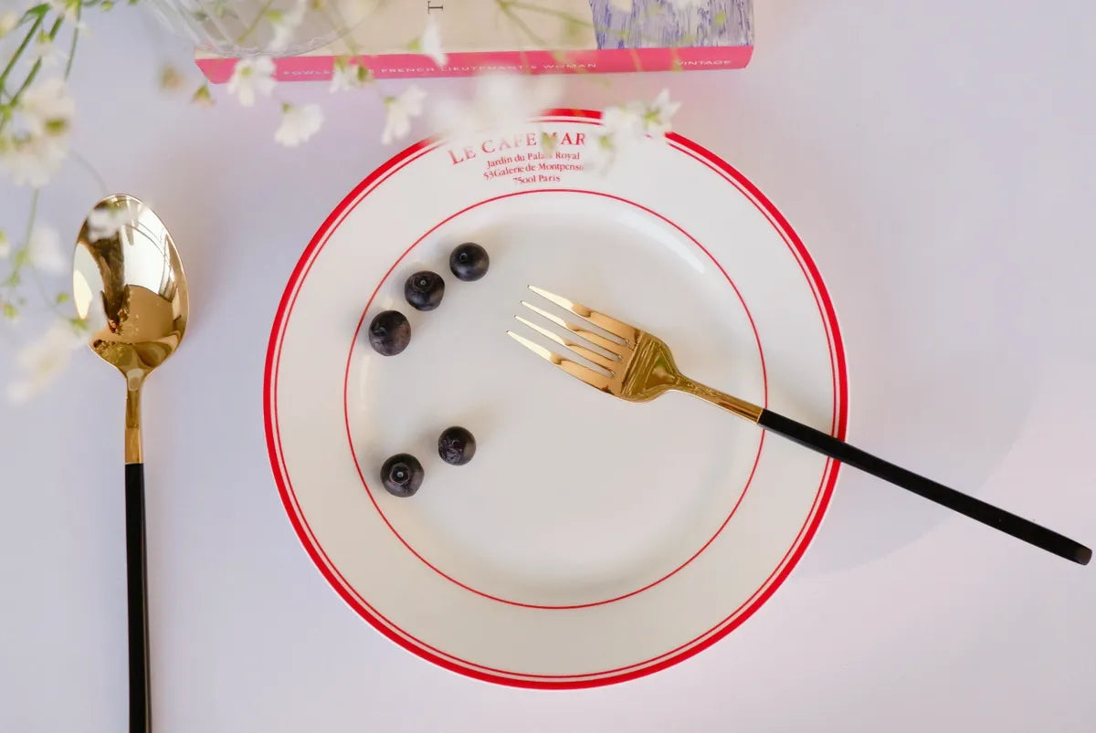 Overhead view of a white bone china quarter plate with double red circular borders and red "Le Cafe Maria" branding