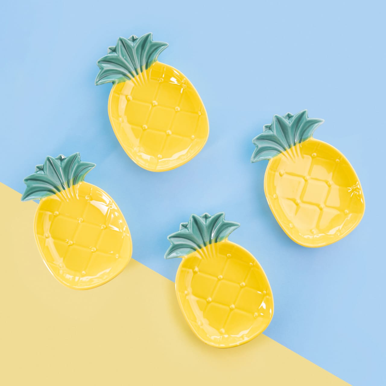 Overhead view of four yellow pineapple-shaped bone china snack plates with green leafy crowns