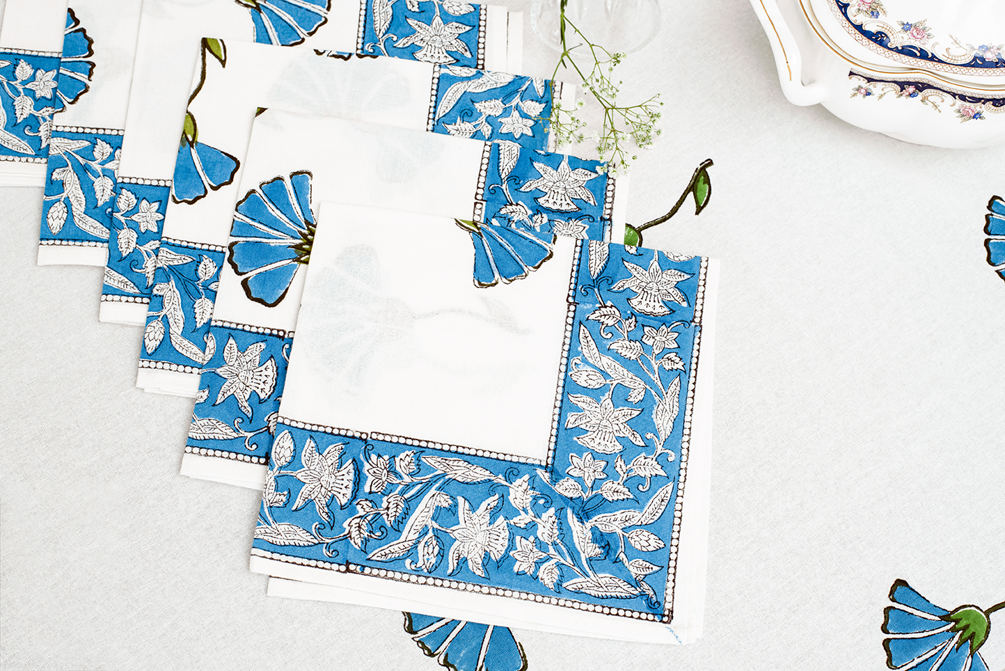 A set of white cotton napkins featuring blue floral block print motifs and an intricate blue patterned border