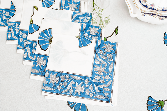 A set of white cotton napkins featuring blue floral block print motifs and an intricate blue patterned border