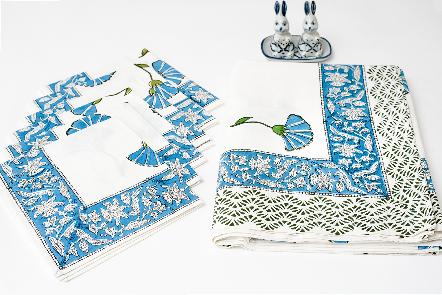A folded white cotton table cloth and matching napkins set featuring traditional blue floral block print motifs and an intricate blue border