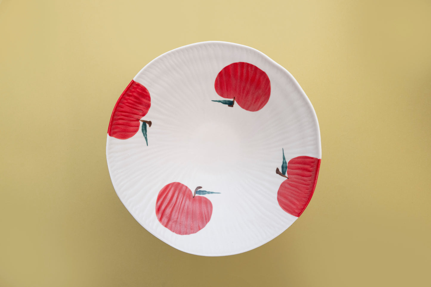 Top view of a white stoneware salad bowl featuring a red apple pattern