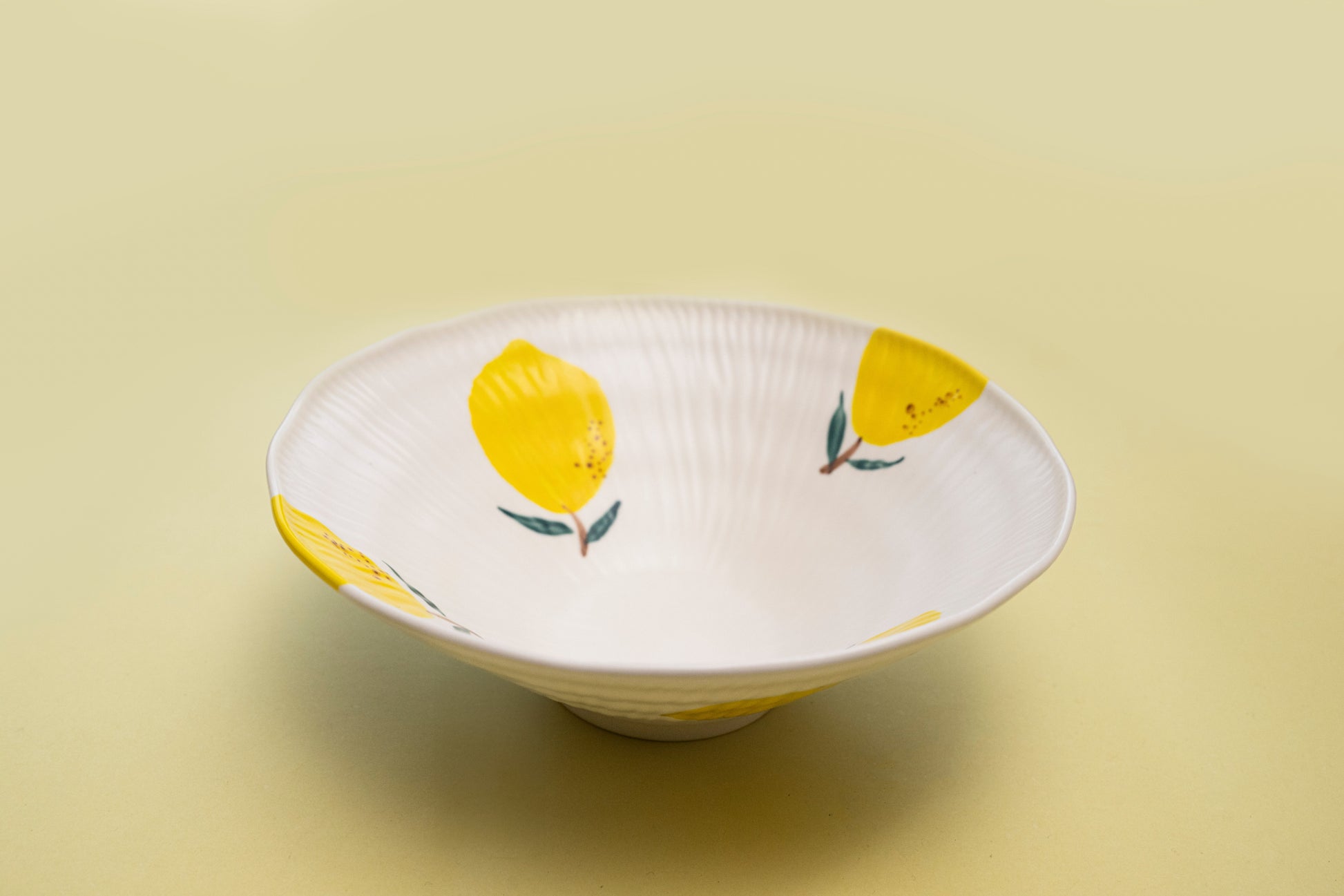 Angled view of a white stoneware salad bowl featuring a yellow lemon pattern