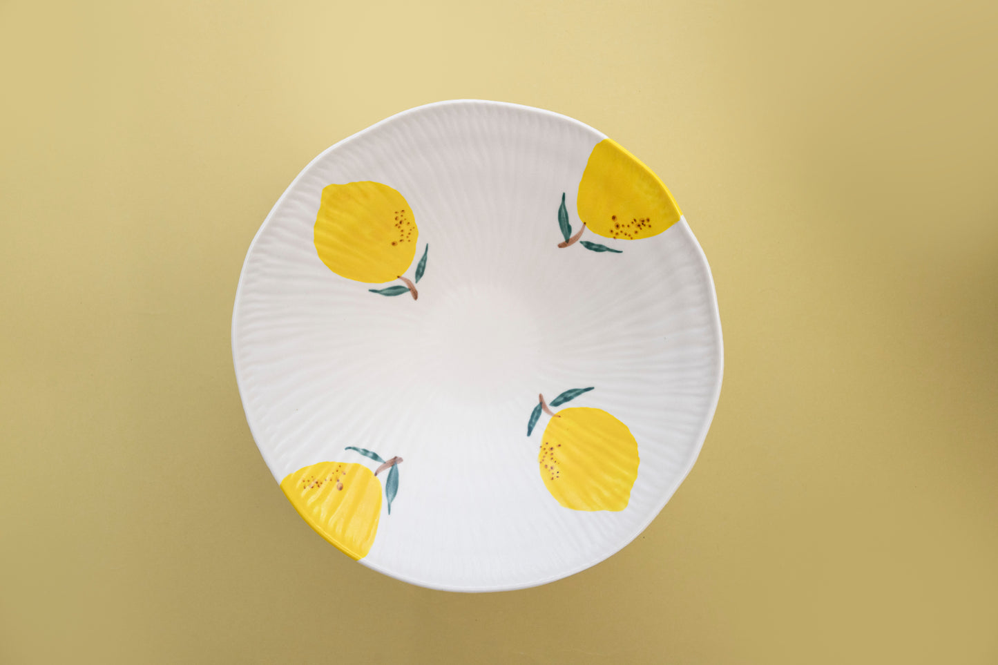 Top view of a white stoneware salad bowl featuring a yellow lemon pattern