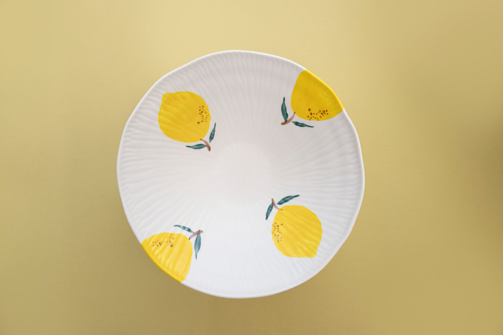Top view of a white stoneware salad bowl featuring a yellow lemon pattern