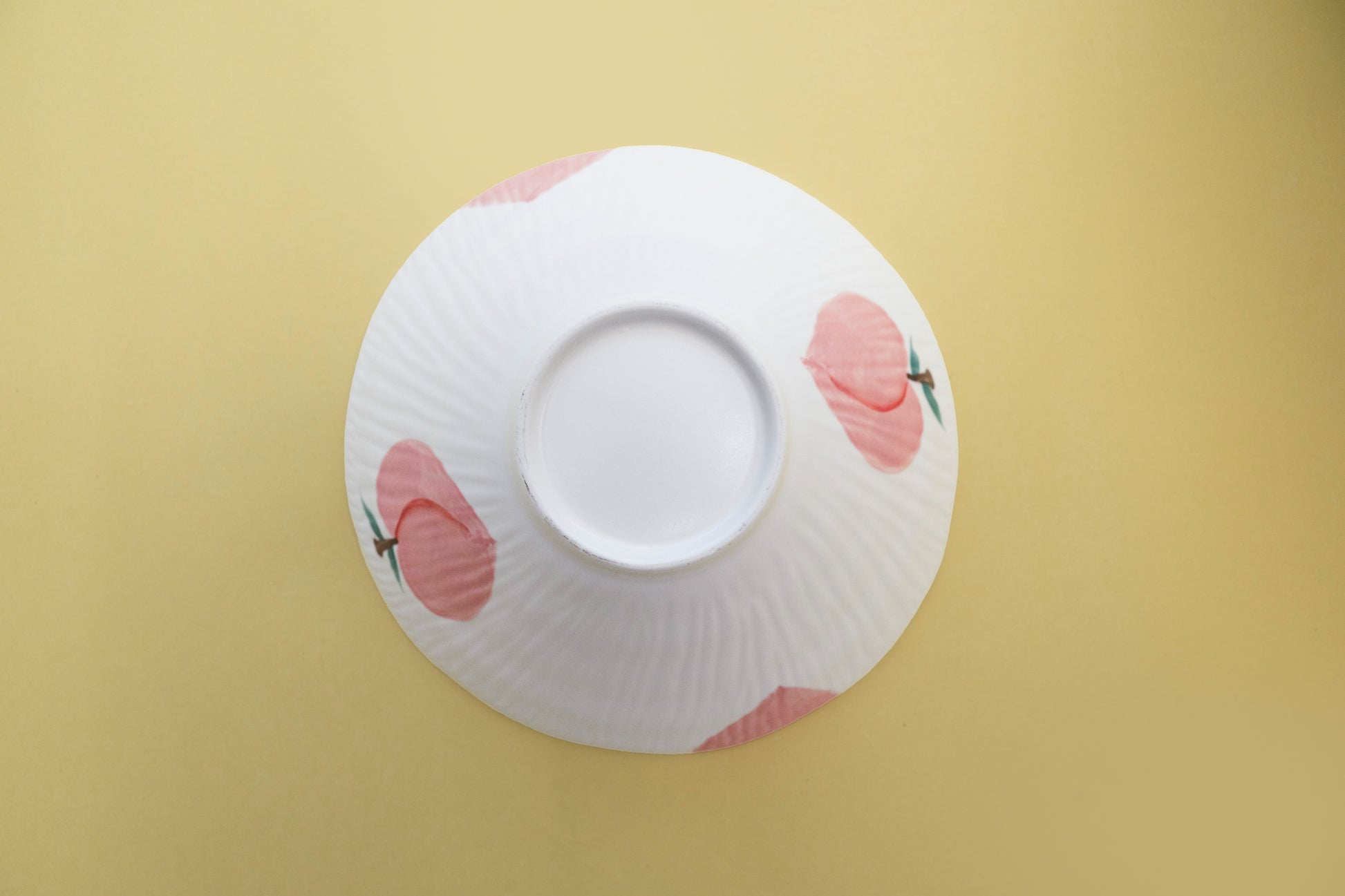 Bottom view of an upside-down white stoneware salad bowl featuring a pink peach pattern