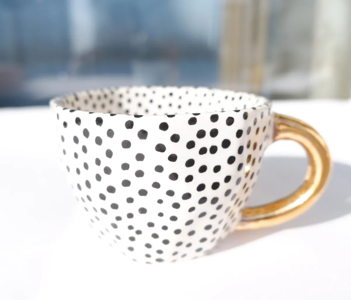 Stoneware mug featuring a black dotty pattern  and a gold handle
