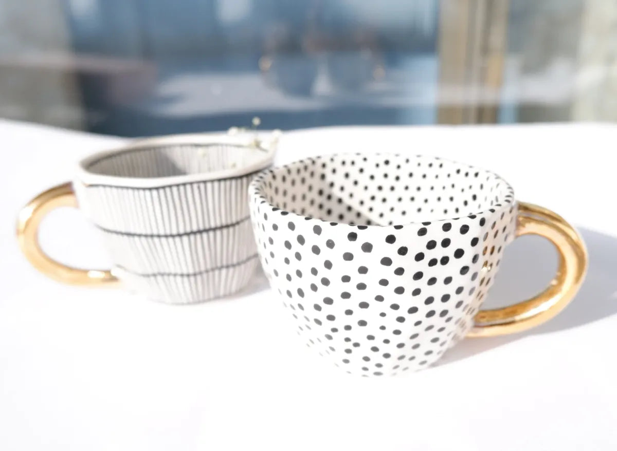 Stoneware mugs featuring black dotty and vertical striped patterns with gold handles