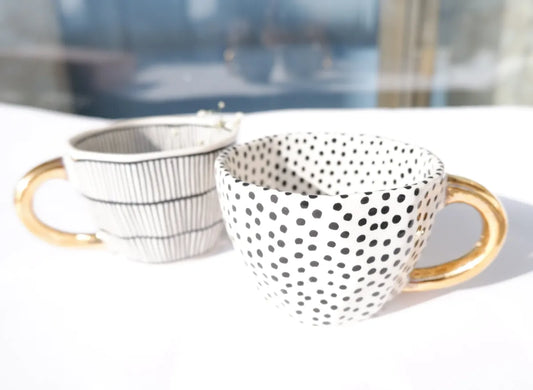 Stoneware mugs featuring black dotty and vertical striped patterns with gold handles