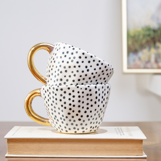 Stoneware mugs featuring a black dotty pattern and gold handles stacked on each other - Birdy Home Design