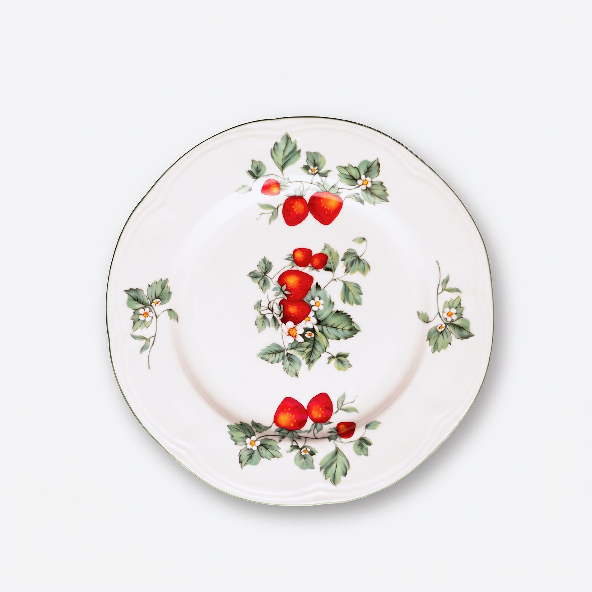 A white ceramic plate featuring a hand-painted strawberry and holly pattern, photographed from directly above on a light gray background.