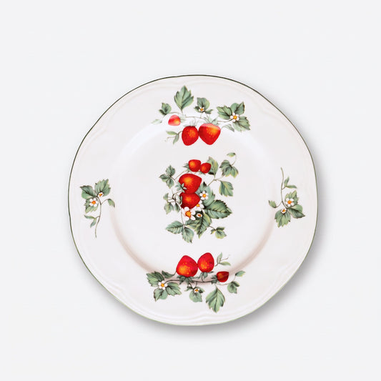 A white ceramic plate featuring a hand-painted strawberry and holly pattern, photographed from directly above on a light gray background.