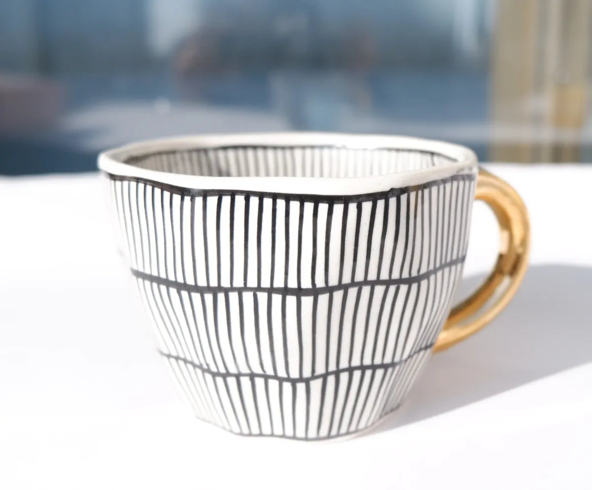 An elegant stoneware mug featuring a hand-painted black and white vertical striped pattern and a metallic gold handle - Birdy Home Design