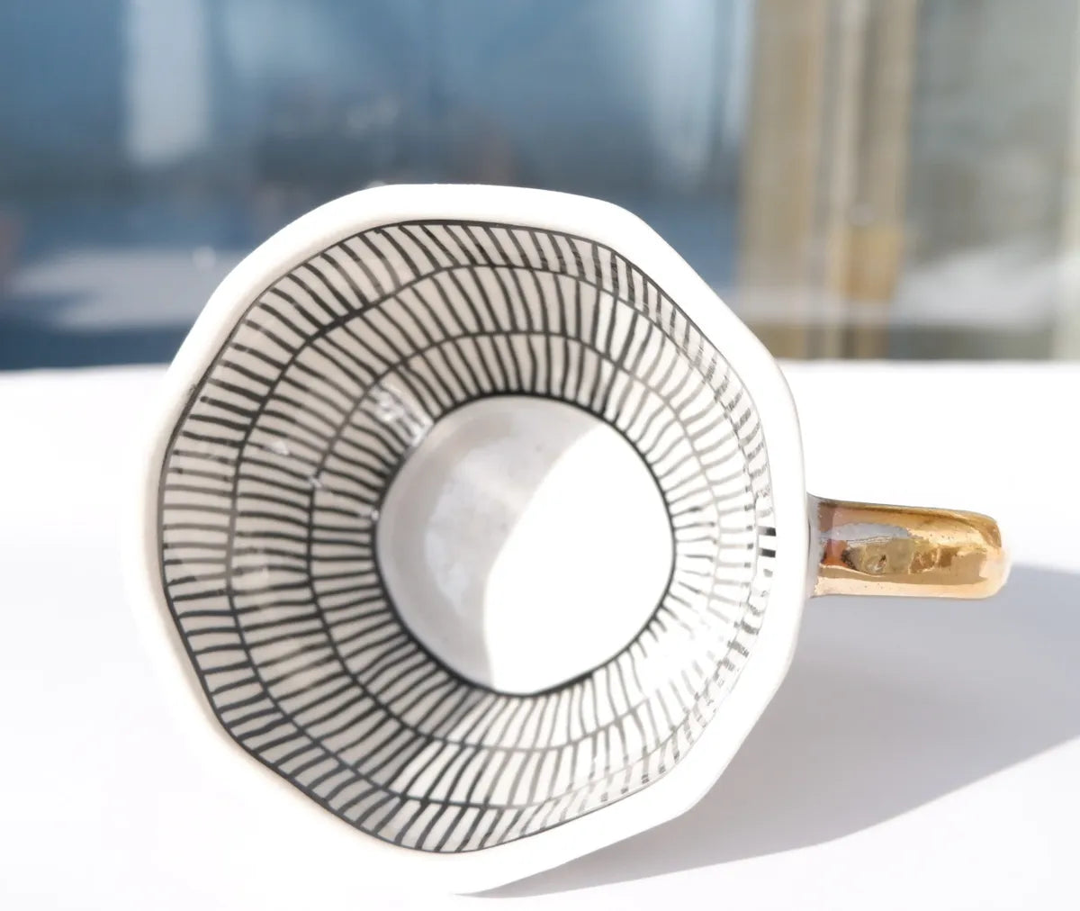 Front-facing view of an elegant stoneware mug with a black and white vertical striped pattern and a contrasting metallic gold handle