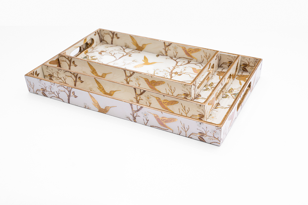 Three white wooden rectangular trays nested together, each featuring gold rims and an intricate gold chinoiserie bird and branch design
